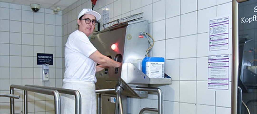 Eine Mitarbeiterin des Bäckereibetriebs hält ihre Hände in eine spezielle Vorrichtung zur Desinfektion der Hände, bevor sie zurück an ihren Arbeitsplatz geht.