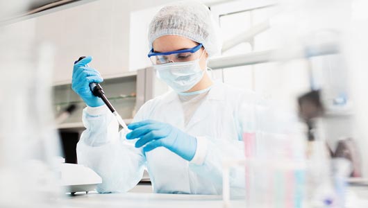 Eine Mitarbeiterin, die im Labor arbeitet. Sie trägt einen Schutzanzug, eine Schutzbrille und Schutzhandschuhe.