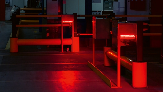 In einem Raum stehen zwei Scanner für Strichcodes an Paletten. Kräftiges rotes Licht erleuchtet den gesamten Raum.