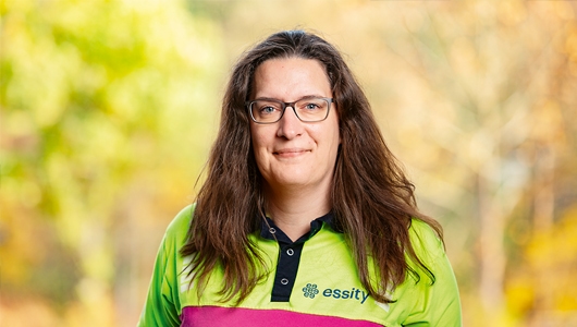 Porträt von Mirjam Wagner, Gesundheitsmanagerin bei Essity am Standort Witzenhausen. Sie hat langes braunes Haar, trägt eine Brille und ein Poloshirt, auf das der Unternehmensname steht.