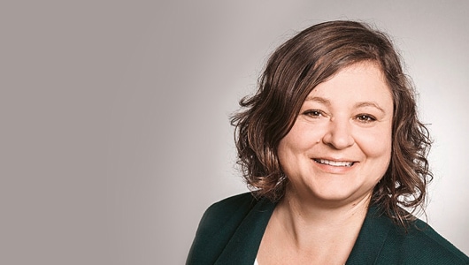 Porträt von Dr. Renate Beisser, Bereichsleiterin für Gefahrstoffexposition, Messtechnik und Bewertung, IFA. Sie hat gelocktes, braunes, schulterlanges Haar und lächelt in die Kamera.