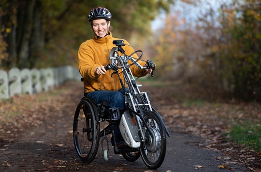 Sabrina Busch trainiert. Sie steht auf einem Weg, mit Helm und in oranger Jacke und Jeans und lächelt in die Kamera.
