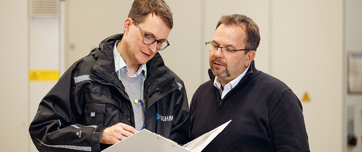 Aufsichtsperson der Berufsgenossenschaft Holz und Metall Marc-Manuel Freitag spricht mit Arbeitssicherheitsfachkraft Rupert Saalwirth. Die beiden Männer schauen gemeinsam in einen Ordner mit Unterlagen.