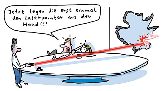 Cartoon, der einen Raum mit drei Personen zeigt. Die Person links steht am Tisch und hat einen Laserpointer in der Hand, der ein großes Loch in die Wand geschossen hat. Die zwei anderen Personen verstecken sich hinter dem Tisch und einer ruft: "Jetzt legen Sie erst einmal den Laserpointer aus der Hand!"
