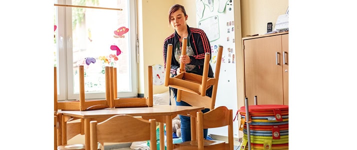 Erzieherin Simone Lorenz stellt in ihrer Kita die Kinderstühle zum Feierabend auf die Tische.