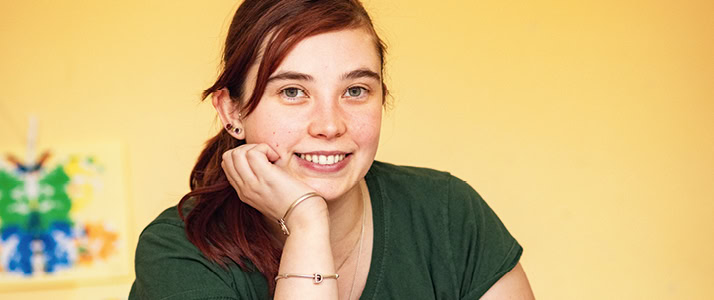 Porträt von Erzieherin Simone Lorenz. Sie lächelt in die Kamera, die dunkelroten Haare tägt sie zum Zopf, außerdem ein dunkelgrünes T-Shirt.
