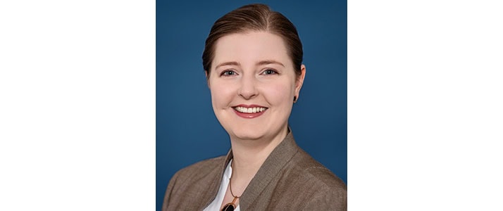 Porträtfoto von Hannah Huxholl von der DGUV. Sie lacht und trägt die dunklen Haare nach hinten gebunden. Sie trägt einen braunen Blazer.
