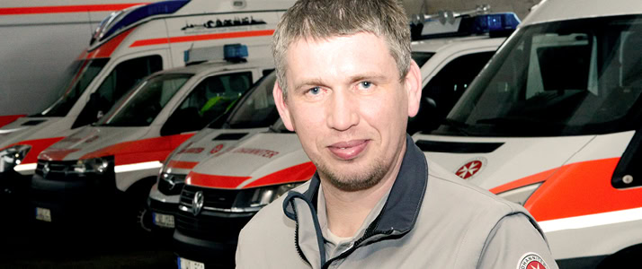 Porträt von Sicherheitsbeauftragtem und zur Leiterprüfung befähigten Person Andreas Rempe. Er steht vor mehreren Einsatzwagen der Johanniter.