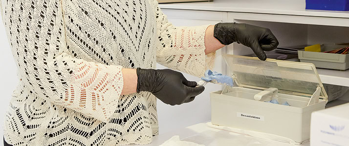 Eine Mitarbeiterin mit Latexhandschuhen legt ein Kunstgebiss in eine Box.