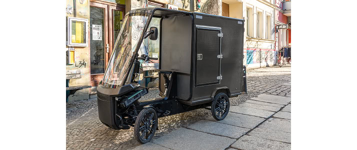 Ein schwarzes, elektrisches Lastenrad mit vier Rädern und Fahrerkabine.