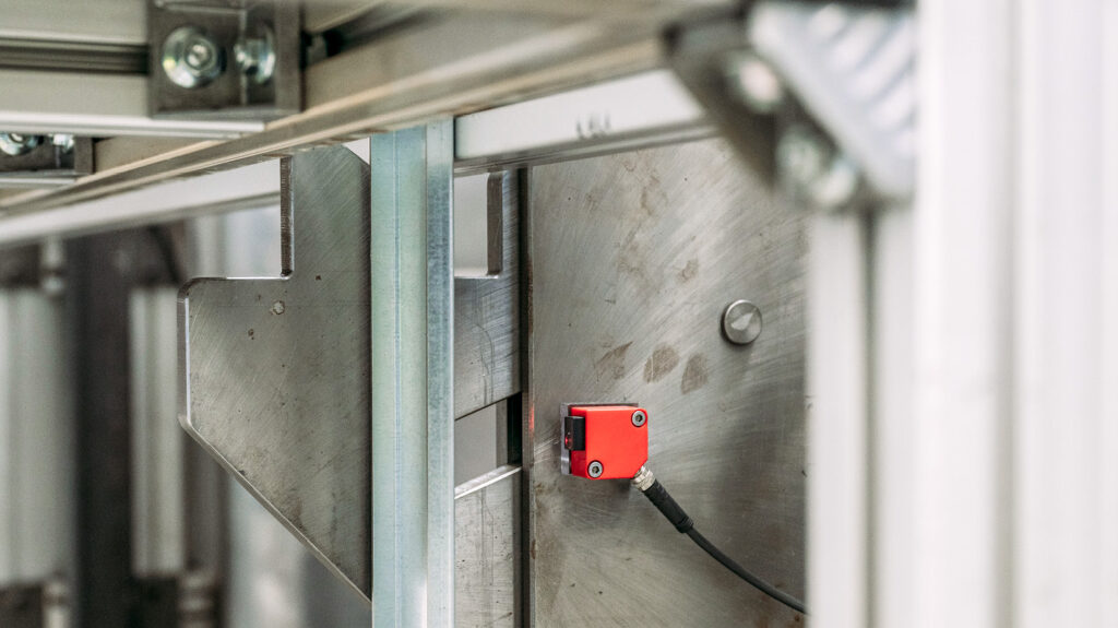 Ein roter Sicherheitsschalter ist am Hubmodul befestigt, aus dem Greifarme aus Metall ausgefahren sind.