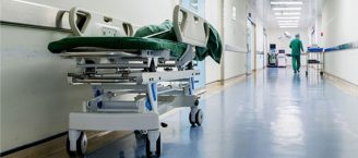 Ein Krankenhausflur mit einer Krankenliege, im Hintergrund ist ein Klinikmitarbeiter in OP-Kleidung zu sehen.