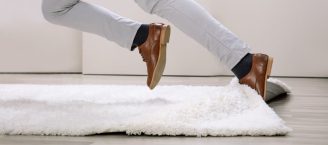 Eine Person stolpert über die Kante eines Teppichs.