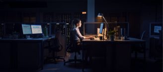 Eine Frau sitzt ein einem Schreibtisch im Büro und arbeitet spätabends am Computer.