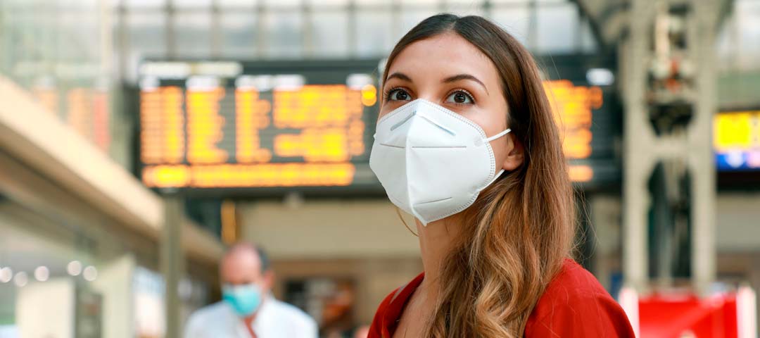 Eine Geschäftsfrau im Flughafengebäude trägt eine FFP2-Maske und wartet auf Informationen zu ihrem Flug.