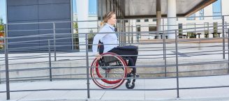 Eine Rollstuhlfahrerin fährt eine Rampe vor einem Gebäude mit ihrem Rollstuhl hoch.