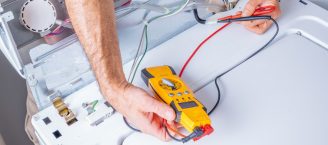 Ein Elektriker ist mit einem gelben Messgerät auf Fehlersuche an einem Haushaltsgerät.
