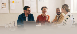 Eine Gruppe fröhlicher Kolleginnen und Kollegen tauscht Ideen aus, während sie gemeinsam in einem hellen Konferenzraum sitzen.