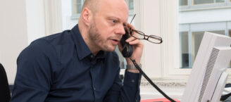 Ein Mann sitzt mit gestresstem Blick am Schreibtisch und telefoniert.
