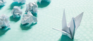 Aus Fehlern lernen: Ein papierner Kranich, nach Origami-Technik gefaltet. Hinter ihm liegen verworfene Kraniche.
