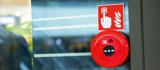 Ein Alarmknopf und ein darüber hängendes Zeichen für Feueralarm hängen an einer Glastür.